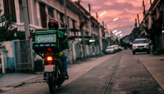 Una persona in moto con in spalla un contenitore per la consegna di cibo a domicilio